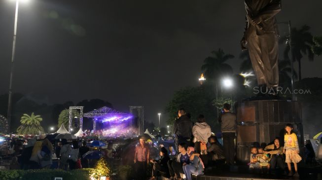 Warga yang sedang beristirahat sejenak saat Car Free Night yang diwarnai hujan, di malam perayaan Tahun Baru 2020 di Jalan Sudirman-Thamrin, Jakarta Pusat, Selasa (31/12/2019). [Suara.com / Alfian Winanto]