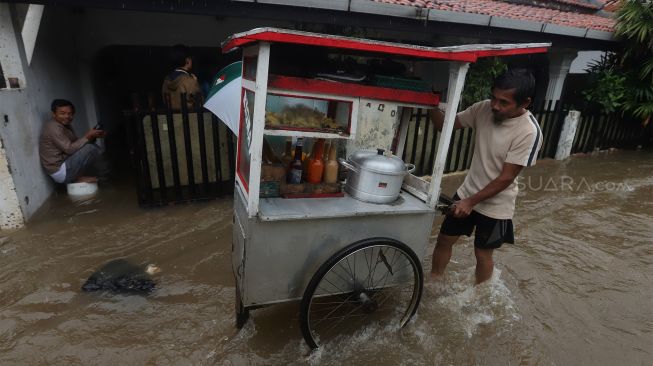 Seorang pedagang melintasi jalan yang terendam banjir di kawasan Jatipadang, Pasar Minggu, Jakarta Selatan, Rabu (1/1). [Suara.com/Angga Budhiyanto]