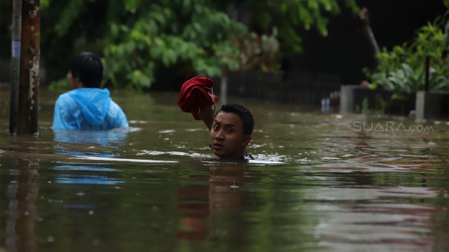 Warga melintasi jalan yang terendam banjir di kawasan Kebon Pala, Jakarta Timur, Rabu (1/1). [Suara.com/Angga Budhiyanto]