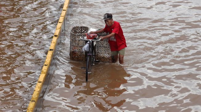 Warga melintasi jalanan yang terendam banjir di Jalan Daan Mogot, Jakarta Barat, Kamis (2/1). [Suara.com/Angga Budhiyanto]
