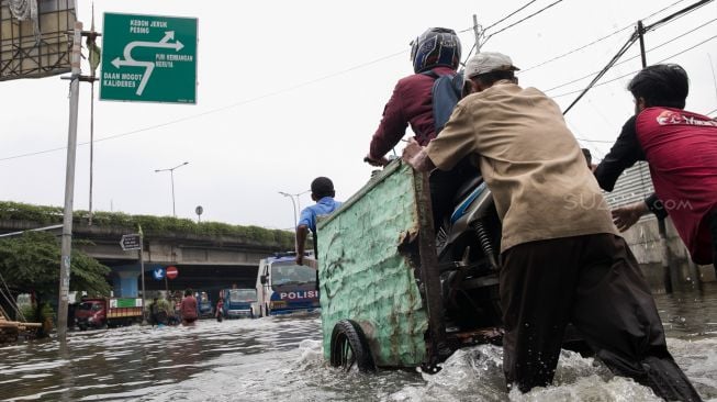 Ojek gerobak mendorong penumpang diatasnya untuk menyeberang Persimpangan Puri Kembangan, Kembangan Pasar Minggu, Jakarta Barat, Jumat (3/1).  [Suara.com/Alfian Winanto]