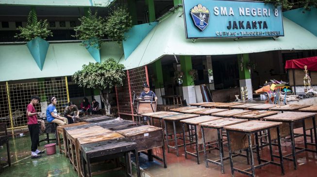 Seorang guru membersihkan meja pascabanjir yang merendam SMA Negeri 8 Jakarta di Bukit Duri, Tebet, Jakarta, Sabtu (4/1).  [ ANTARA FOTO/Aprillio Akbar]