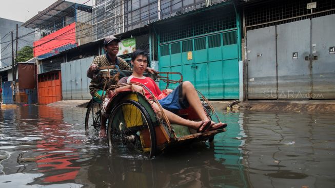 Pengayuh becak membawa penumpang menerobos banjir di Kawasan Teluk Gong, Penjaringan, Jakarta Utara, Sabtu (4/1). [Suara.com/Alfian Winanto]