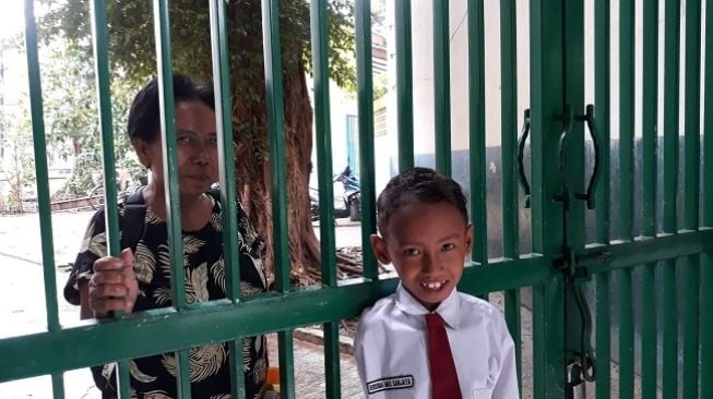 Sri, salah satu wali murid mengantar anaknya masuk sekolah di SDN 01 Pasar Baru, meski menjadi korban banjir Jakarta. (Suara.com/Novian Ardiansyah)