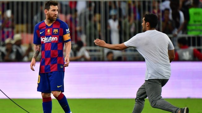Megabintang Barcelona, Lionel Messi (kiri) dihampiri oleh penonton yang merangsek masuk ke lapangan, pada laga Piala Super Spanyol kontra Atletico Madrid di King Abdullah Sports City, Jeddah, Arab Saudi, Jumat (10/1/2020) dini hari WIB. [Giuseppe CACACE / AFP]