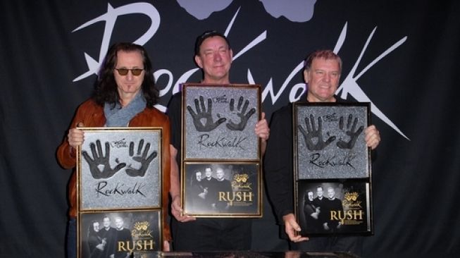 Formasi lengkap grup musik rock progresif dan heavy metal asal Kanada, RUSH: Geddy Lee (kiri), Neil Peart (tengah), dan Alex Lifeson saat digelar RUSH Induction Into Guitar Center's RockWalk, Guitar Center, Los Angeles, California, Amerika Serikat, 2012 [Shutterstock].