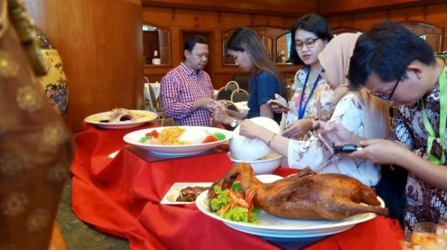 Pengunjung sedang memotret menu spesial Bebek Panggang di Cafe Sirih. (Suara.com/Silfa Humairah)