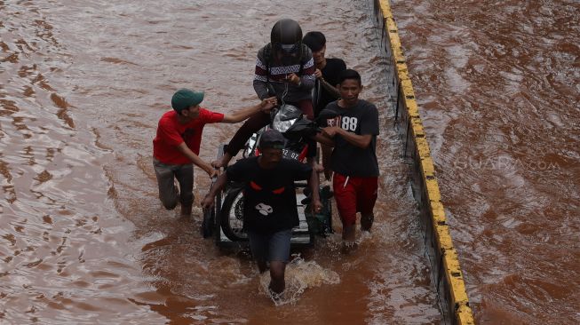 Pengendara menuntun motornya yang mogok melintasi banjir di Jalan Daan Mogot, Jakarta Barat, Kamis (2/1). [Suara.com/Angga Budhiyanto]