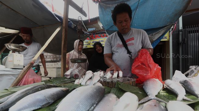 Pedagang ikan bandeng melayani pembeli di Pasar Rawa Belong, Jakarta Barat, Rabu (22/1). [Suara.com/Angga Budhiyanto]
