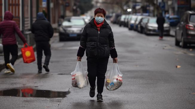 Seorang wanita yang mengenakan masker wajah usai kembali dari pasar di Wuhan, Cina, Minggu (26/1). [Hector RETAMAL / AFP]