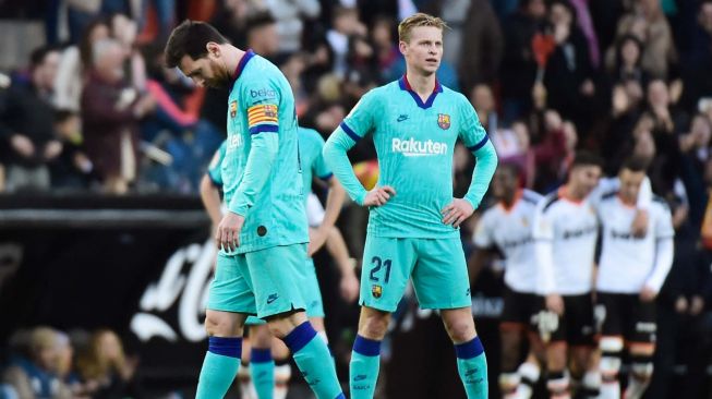 Pemain depan Barcelona Lionel Messi dan gelandang Barcelona Frenkie De Jong tertunduk lesu usai timnya dikalahkan oleh Valencia selama pertandingan sepak bola liga Spanyol Valencia melawan Barcelona di Stadion Mestalla, Valencia, Spanyol, Sabtu (26/1). [JOSE JORDAN / AFP]