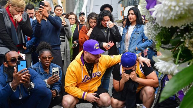 Penggemar Kobe Bryant berduka saat berkumpul di depan Staples Center, Los Angeles Lakers, Amerika, Minggu (26/1). [Frederic J. Brown / AFP]