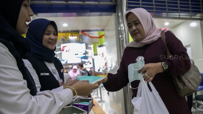 Petugas membagi-bagikan masker gratis kepada penumpang kereta api di Stasiun Gambir, Jakarta Pusat, Jumat (31/01). [Suara.com/Alfian Winanto]
