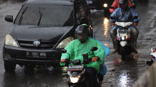 Pengendara motor yang mengenakan jas hujan saat melewati daerah kuningan, Jakarta Selatan, Sabtu (01/02). [Suara.com/Alfian Winanto]