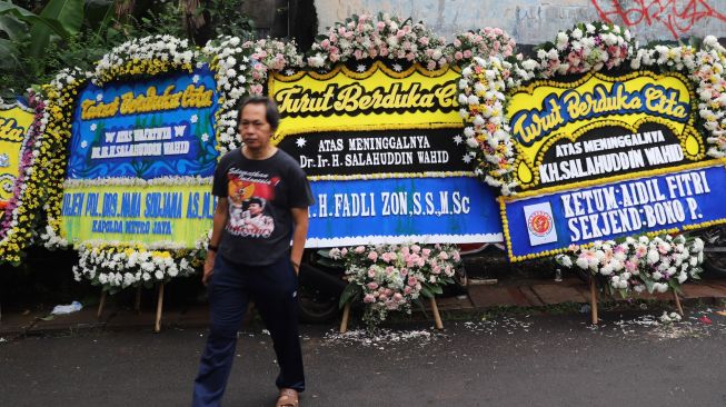 Sejumlah pelayat melintas di depan karangan bunga ucapan belasungkawa atas wafatnya KH Salahuddin Wahid atau Gus Sholah di rumah duka di kawasan Mampang Prapatan, Jakarta, Senin (3/2).[Suara.com/Alfian Winanto]