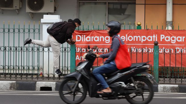 Penumpang KRL menaiki pagar pembatas trotoar di Stasiun Cikini, Jakarta, Rabu (5/2). [Suara.com/Angga Budhiyanto]
