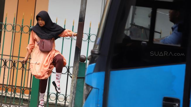 Penumpang KRL menaiki pagar pembatas trotoar di Stasiun Cikini, Jakarta, Rabu (5/2). [Suara.com/Angga Budhiyanto]
