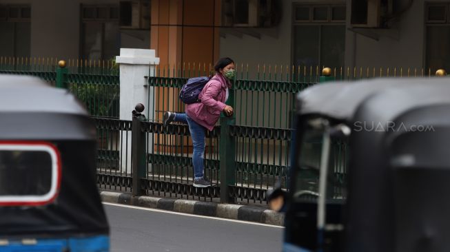 Penumpang KRL menaiki pagar pembatas trotoar di Stasiun Cikini, Jakarta, Rabu (5/2). [Suara.com/Angga Budhiyanto]
