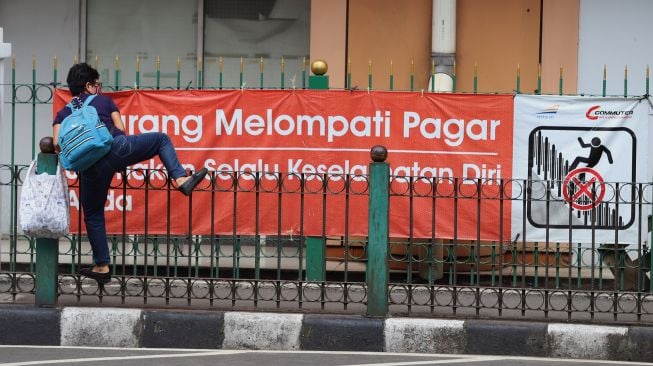 Penumpang KRL menaiki pagar pembatas trotoar di Stasiun Cikini, Jakarta, Rabu (5/2). [Suara.com/Angga Budhiyanto]
