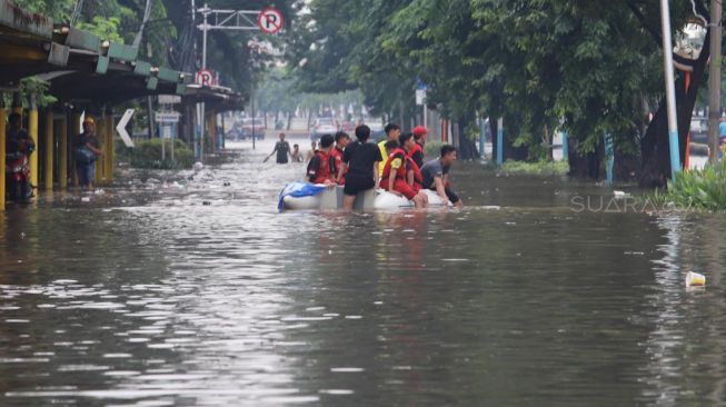 Warga menaiki perahu karet ke untuk ke area yang tergenang cukup dalam di Jalan Cempaka Putih, Jakarta Pusat, Sabtu (08/02).[Suara.com/Alfian Winanto]
