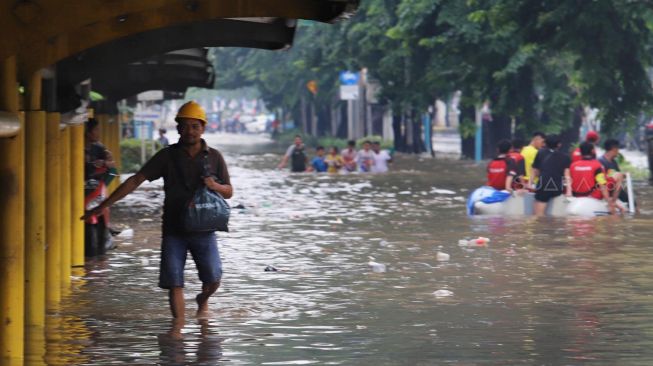 Warga melintasi genangan banjir di Jalan Cempaka Putih, Jakarta Pusat, Sabtu (08/02).[Suara.com/Alfian Winanto]
