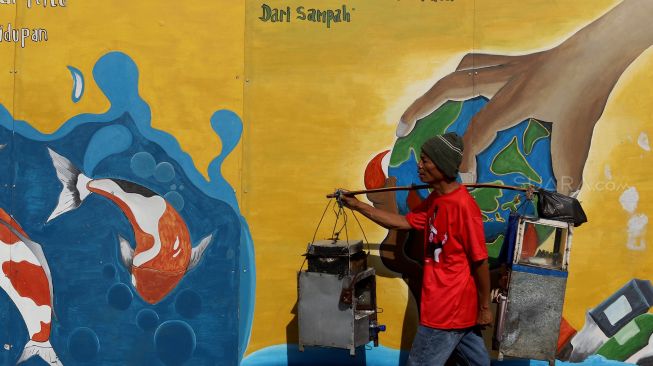 Seorang warga melintas di depan mural yang berisi pesan ajakan untuk menjaga lingkungan di Jalan Tambak, Manggarai, Jakarta, Senin (10/2). [Suara.com/Angga Budhiyanto]