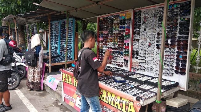 Seorang penjual kacamata di Simpang Lima UNY menata barang dagangannya, Selasa (11/2/2020). - (Suara.com/Baktora)