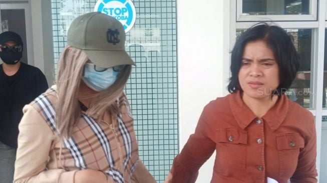 Lucinta Luna (mengenakan kemeja cokelat, topi dan masker) bersama petugas kepolisian di Polres Jakarta Barat. [Herwanto/Suara.com]