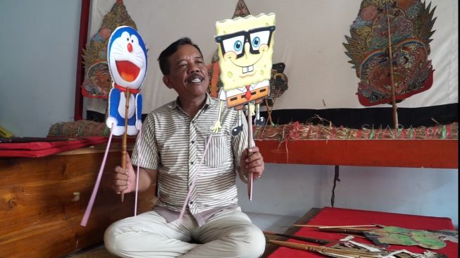 Dalang wayang Jawa Timuran, Ki Puguh Prasetyo dengan beberapa figur wayangnya yang berasal dari tokoh kartun populer. [Suara.com / Arry Saputra]