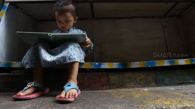 Seorang anak membaca di Taman Bacaan di kawasan Jembatan Lima, Jakarta,  Kamis (13/2). [Suara.com/Angga Budhiyanto]