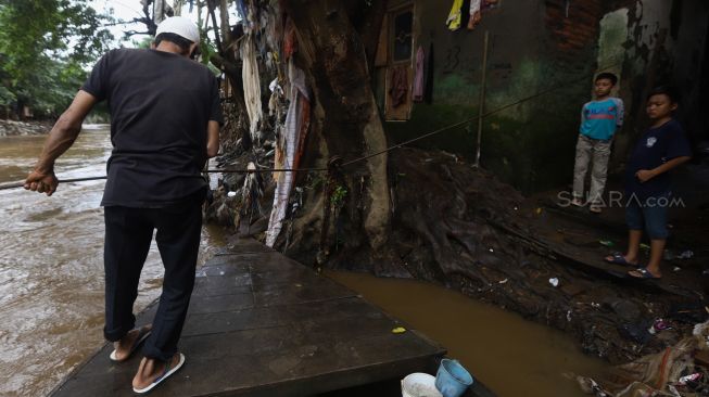 Seorang warga mengoperasikan perahu eretan untuk menyeberangi Kali Ciliwung di kawasan Manggarai, Jakarta, Jumat (14/2). [Suara.com/Angga Budhiyanto]