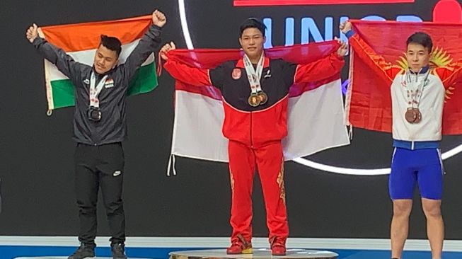 Lifter muda Indonesia, Muhammad Faathir (tengah) berhasil meraih tiga medali emas sekaligus memecahkan dua rekor dunia remaja di kelas 61kg saat turun di Kejuaraan Angkat Besi Junior Asia 2020 di Uzbekistan Sports Complex, Uzbekistan, Sabtu (15/2/2020). [Istimewa]