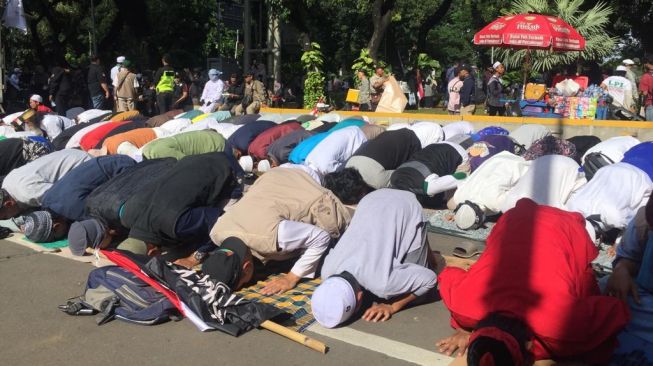 Peserta aksi 212 melaksanakan ibadah Salat Ashar di bawah Jembatan Penyeberangan Orang (JPO) yang berada di Gedung Sapta Pesona, Jalan Medan Merdeka Barat. [Suara.com/Yosea Arga P]