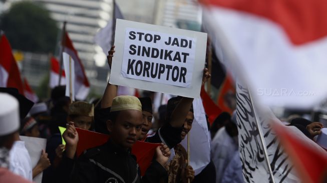 Massa aksi membawa poster bertuliskan 'Stop Jadi Sindikat Koruptor' saat aksi unjuk rasa terkait "Berantas Mega Korupsi, Selamatkan NKRI" di Jalan Merdeka Barat, Jakarta, Jumat (21/2). [Suara.com/Angga Budhiyanto]