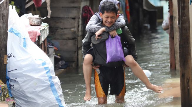 Seorang suami menggendong istrinya melewati banjir banjir di Petamburan II, Jakarta Pusat, Minggu (23/02).  [Suara.com/Alfian Winanto]