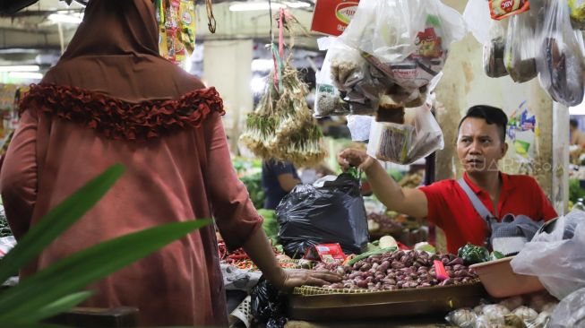 Pedagang memberikan kantong plastik yang berisi barang belanjaan pembeli  di Pasar Tradisional Pasar Minggu, Jakarta Selatan, Senin (24/02). [Suara.com/Alfian Winanto]

