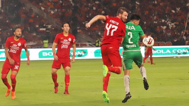 Duel perebutan bola antara Defender Persija Marco Motta dengan Defender Geylang International FC Kamolidin Tashiev dalam laga persahabatan di Stadion Utama Gelora Bung Karno, Jakarta, Minggu (24/02). [Suara.com/Alfian Winanto]