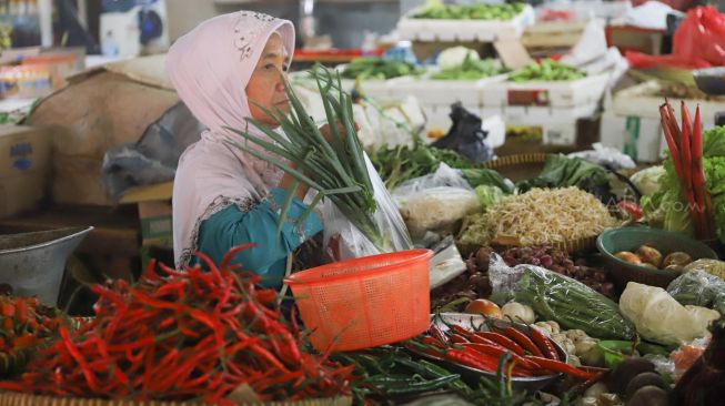 Pedagang membungkus sayuran jualannya kedalam kantong plastik di Pasar Tradisional Pasar Minggu, Jakarta Selatan, Senin (24/02). [Suara.com/Alfian Winanto]