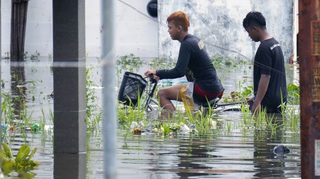 Warga melewati jalan desa yang terendam banjir di Tirto, Pekalongan, Jawa Tengah, Senin (24/2). [ANTARA FOTO/Harviyan Perdana Putra]