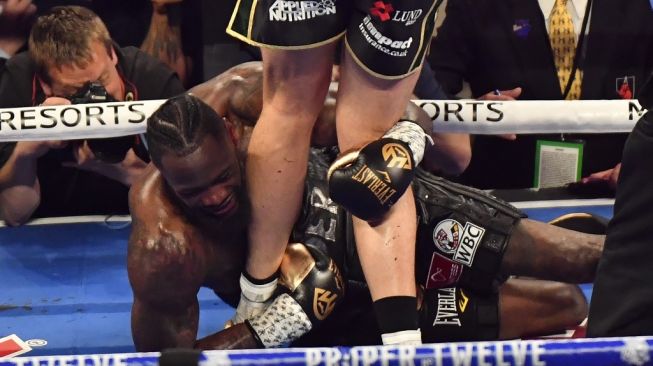 Petinju AS Deontay Wilder memegang kaki penantangnya, Tyson Fury, usai dipukul jatuh dalam duel di MGM Grand Garden Arena, Las Vegas, Sabtu (22/2/2020). [AFP/Mark Ralston]