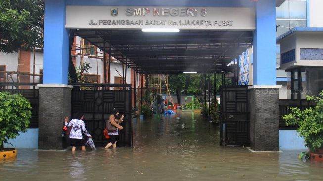 Dua orang guru melintasi banjir yang menggenangi sekolah SMPN 8, Jakarta, Selasa (25/2).  [Suara.com/Oke  Atmaja]