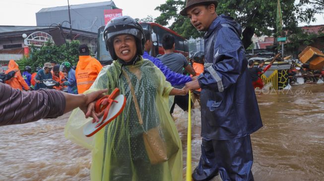 Warga yang menyebrangi derasnya banjir dengan bantuan tali di Jalan Raya Pondok Gede, Bekasi, Jawa Barat, Selasa (25/02). [Suara.com/Alfian Winanto]