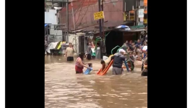 Tak peduli dengan banjir yang menggenang tinggi, warga mencari kesenangan lain ditengah bencana dengan memasang perosotan.