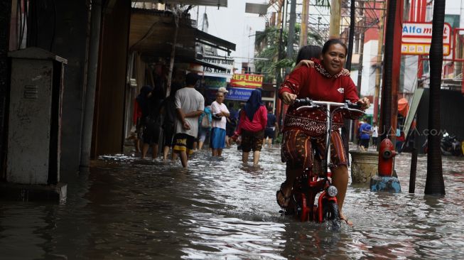 Warga menggunakan sepeda melintasi banjir yang merendam kawasan Pasar Baru, Jakarta Pusat, Selasa (25/2). [Suara.com/Angga Budhiyanto]