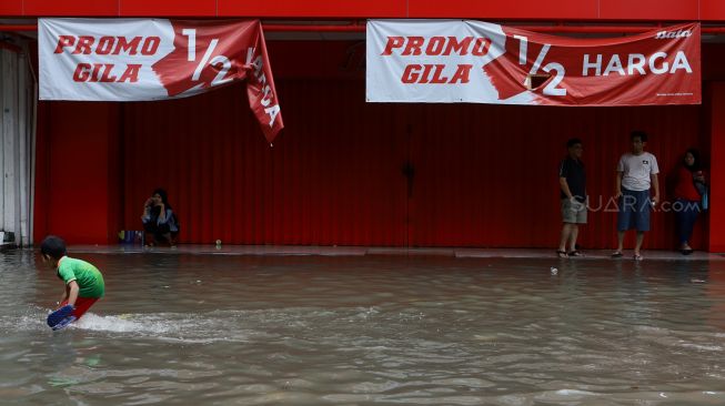 Seorang anak melintasi banjir yang merendam kawasan Pasar Baru, Jakarta Pusat, Selasa (25/2). [Suara.com/Angga Budhiyanto]