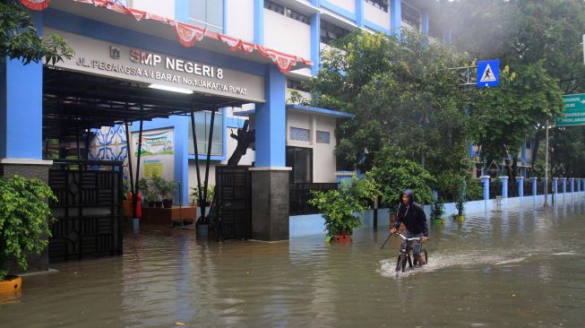 Warga naik sepeda melintasi banjir yang menggenangi sekolah SMPN 8, Jakarta, Selasa (25/2). [Suara.com/Oke  Atmaja]
