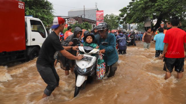 Warga membantu motor mogok melewati banjir di Jalan Raya Pondok Gede, Bekasi, Jawa Barat, Selasa (25/02). [Suara.com/Alfian Winanto]