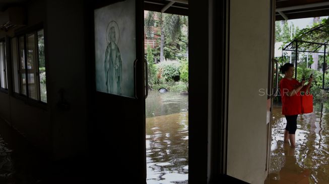 Seorang warga memotret Gereja Santo Kristoforus yang terendam banjir di kawasan Jalan Satria IV, Kelurahan Jelambar, Jakarta Barat, Selasa (25/2). [Suara.com/Angga Budhiyanto]  