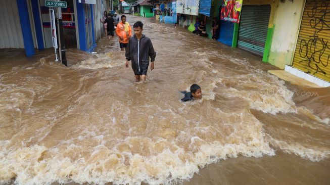 Bocah berenang saat banjir di Jalan Raya Pondok Gede, Bekasi, Jawa Barat, Selasa (25/02). [Suara.com/Alfian Winanto]