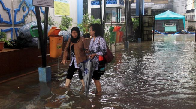 Dua orang guru melintasi banjir yang menggenangi sekolah SMPN 8, Jakarta, Selasa (25/2).  [Suara.com/Oke  Atmaja]